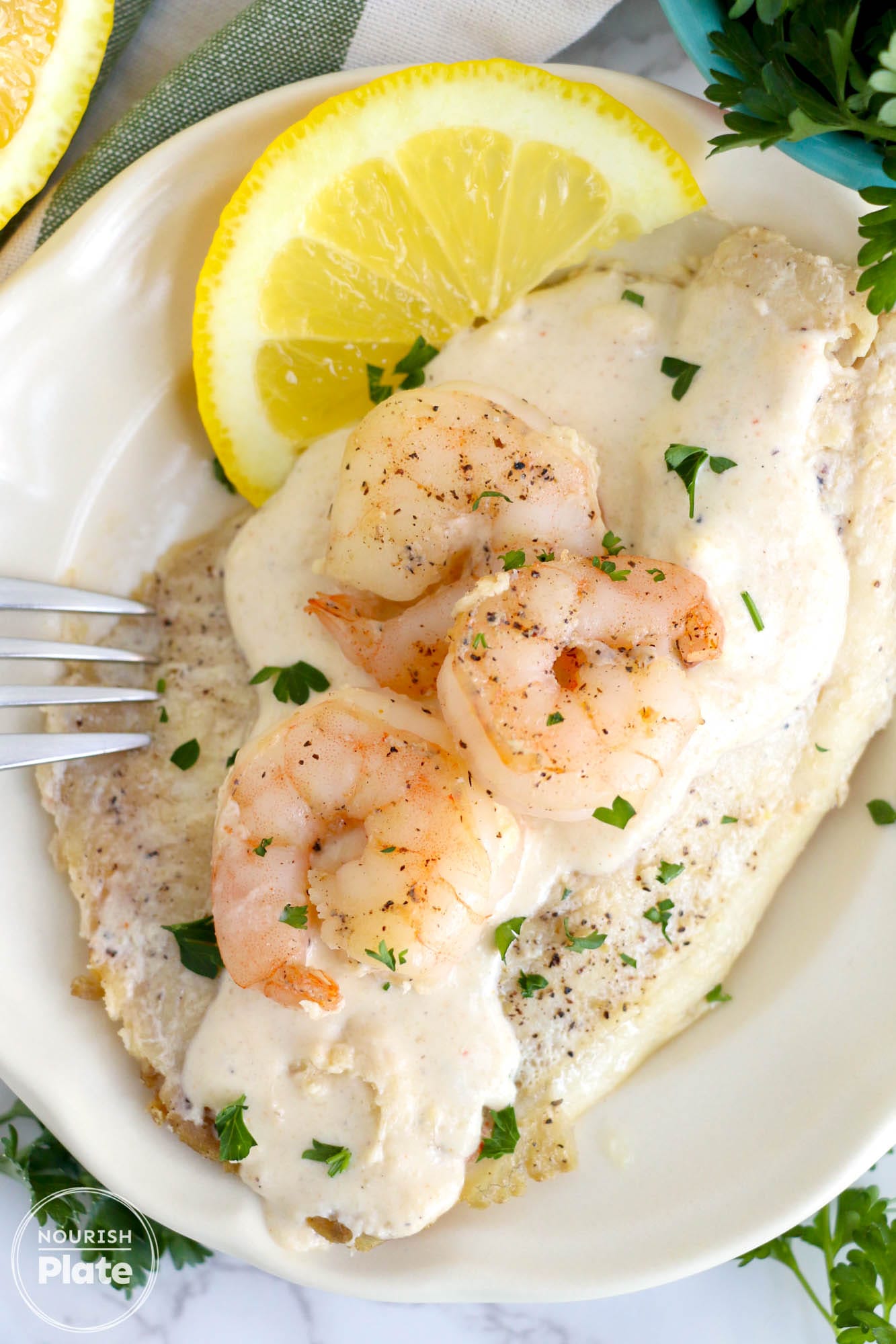 Pan Seared Tilapia and Shrimp on a plate, with a creamy sauce, and fresh lemon slices