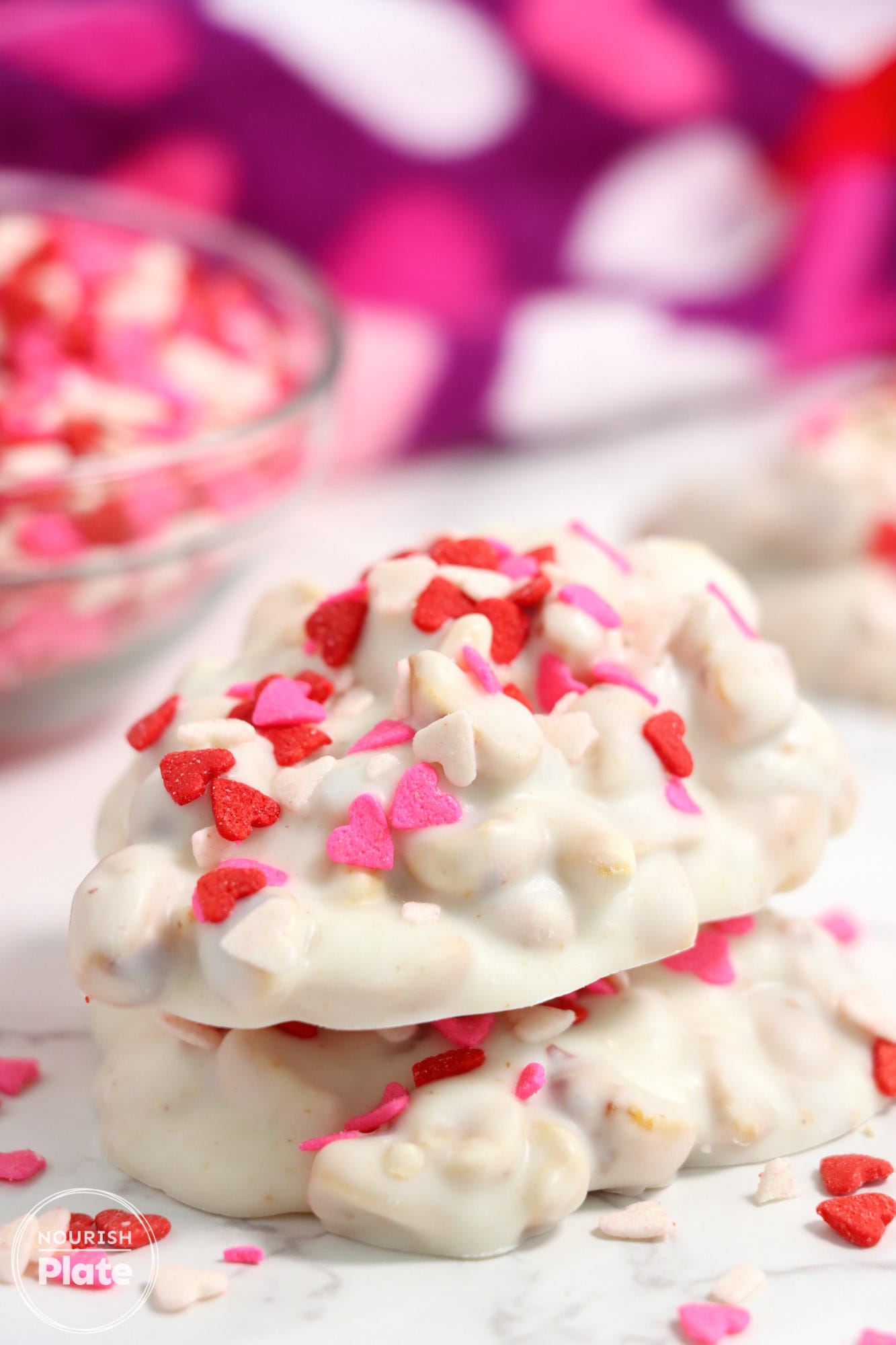 2 pieces of white chocolate crockpot candy stacked, topped with valentine's day candy.