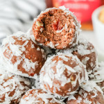 Close-up of chocolate Amaretto balls coated in shredded coconut, stacked in a bowl with one ball bitten open to reveal a nutty chocolate interior and a cherry piece inside.