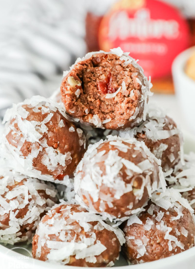 Close-up of chocolate Amaretto balls coated in shredded coconut, stacked in a bowl with one ball bitten open to reveal a nutty chocolate interior and a cherry piece inside.