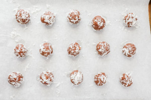 Chocolate Amaretto balls coated in shredded coconut, evenly spaced on a parchment-lined baking sheet, ready to chill.
