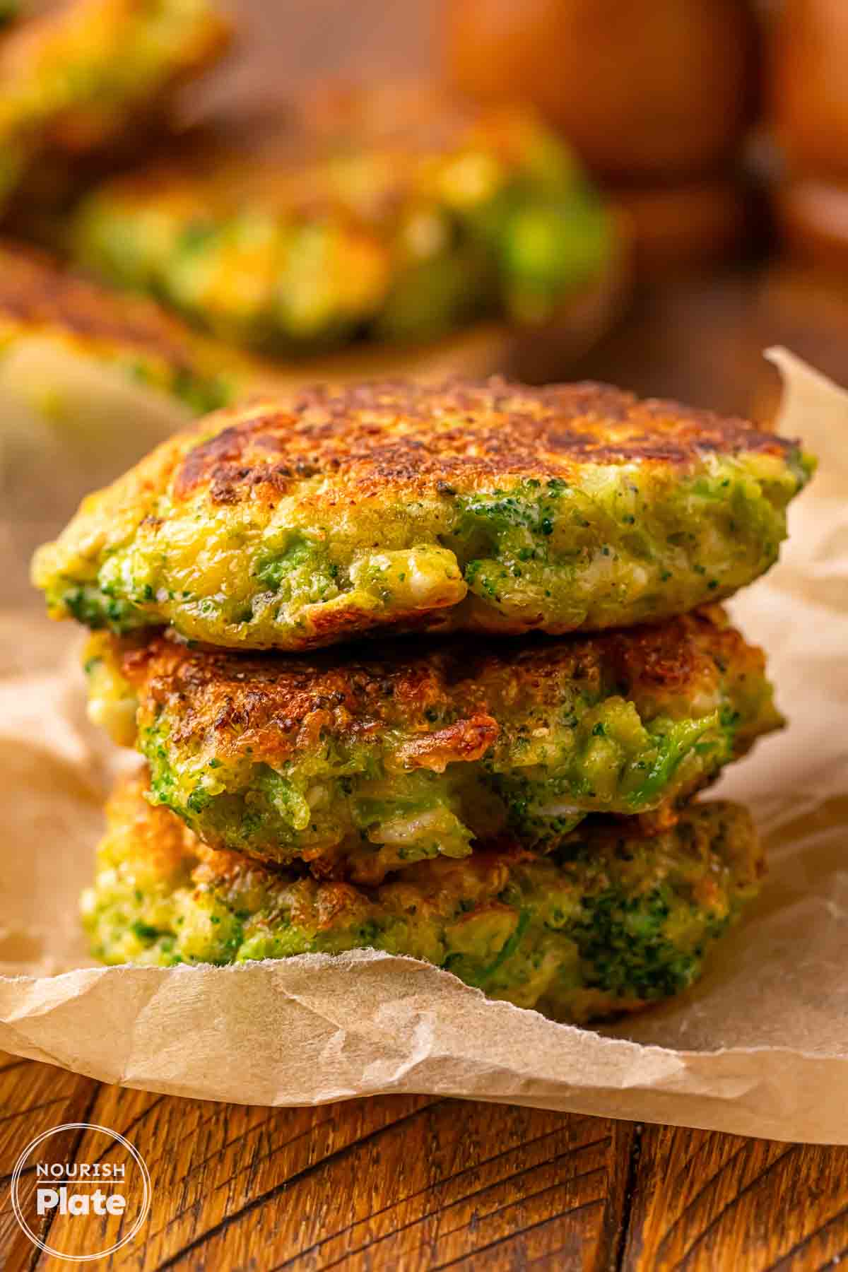 3 golden broccoli fritters stacked on a piece of parchment paper