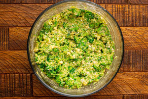 Broccoli fritter mixture fully mixed in a glass bowl with finely chopped broccoli, feta cheese, eggs, flour, and seasonings.