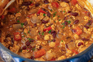 Close up of Cajun chicken and kidney beans simmering in a thick sauce with onions and red bell pepper in a Dutch oven.