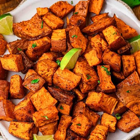 Roasted sweet potato cubes seasoned with chili and smoked paprika on a white plate, garnished with lime wedges and chopped cilantro.
