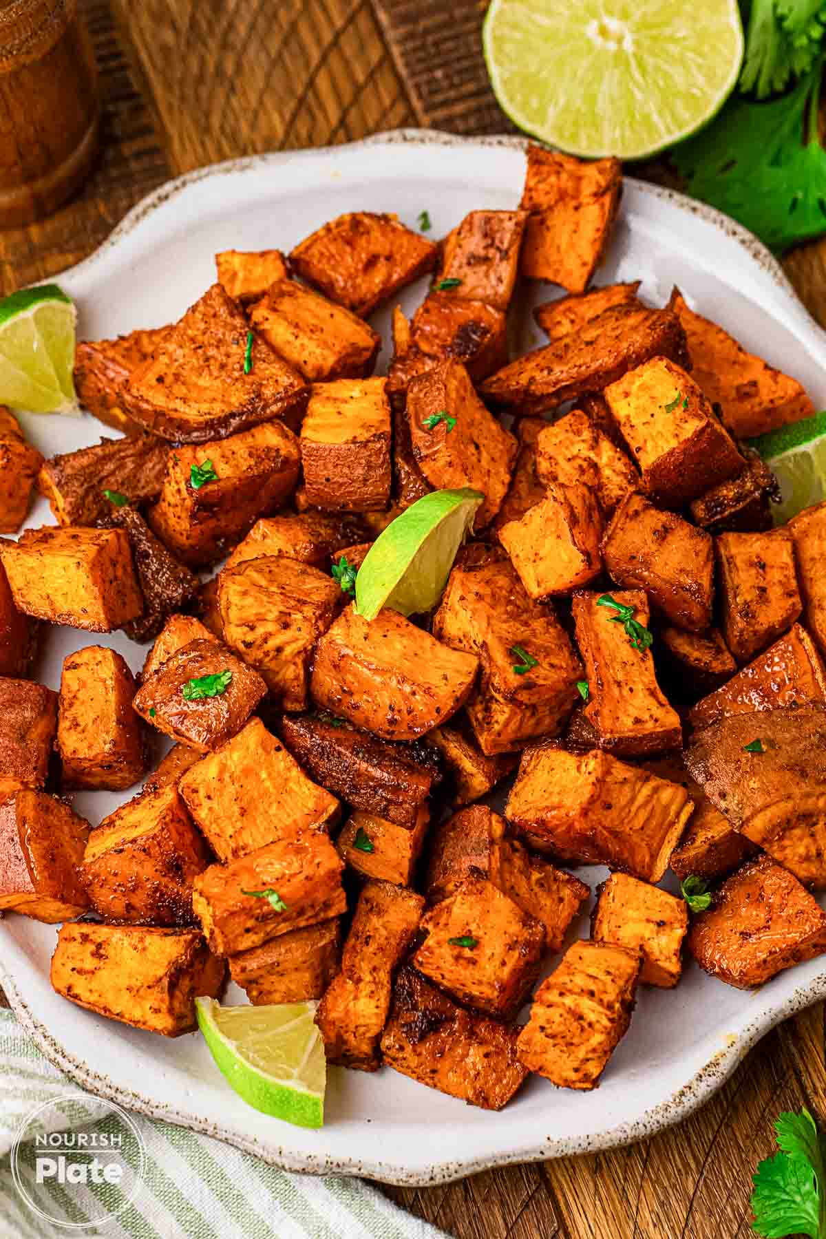 Roasted sweet potato cubes seasoned with chili and smoked paprika on a white plate, garnished with lime wedges and chopped cilantro.