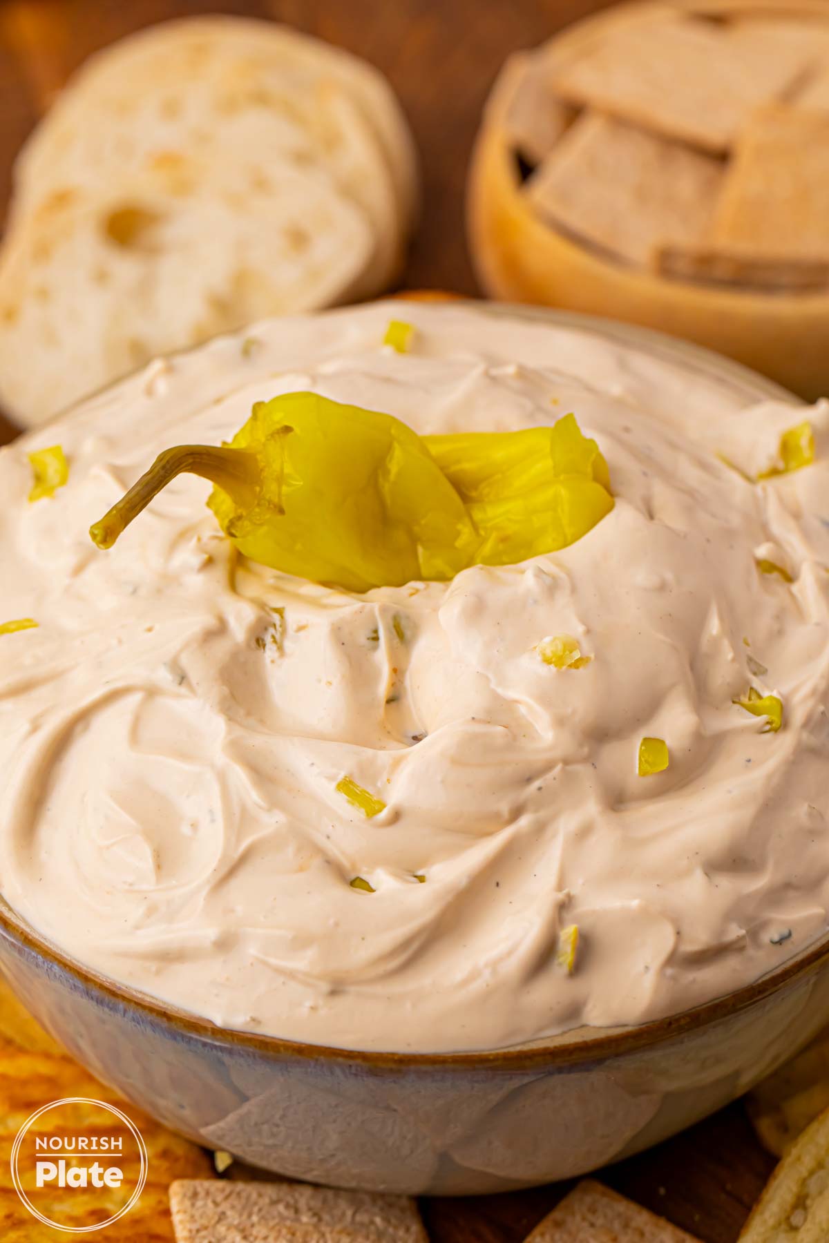 Mississippi Sin Dip in a serving bowl topped with a whole pepperoncini, with crackers and bread in the background