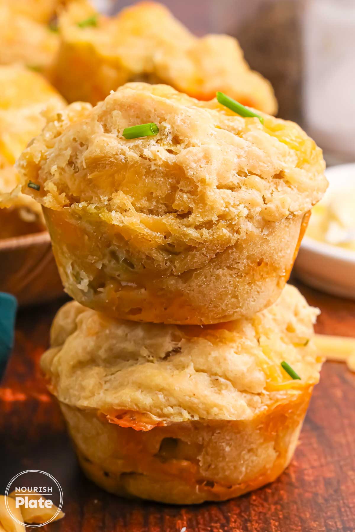 Stack of two beer cheese bread muffins with melted cheddar, green chiles, and chives, shown close up on a wooden surface.