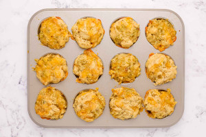 Freshly baked beer cheese bread muffins in a muffin pan with golden tops and melted cheddar.