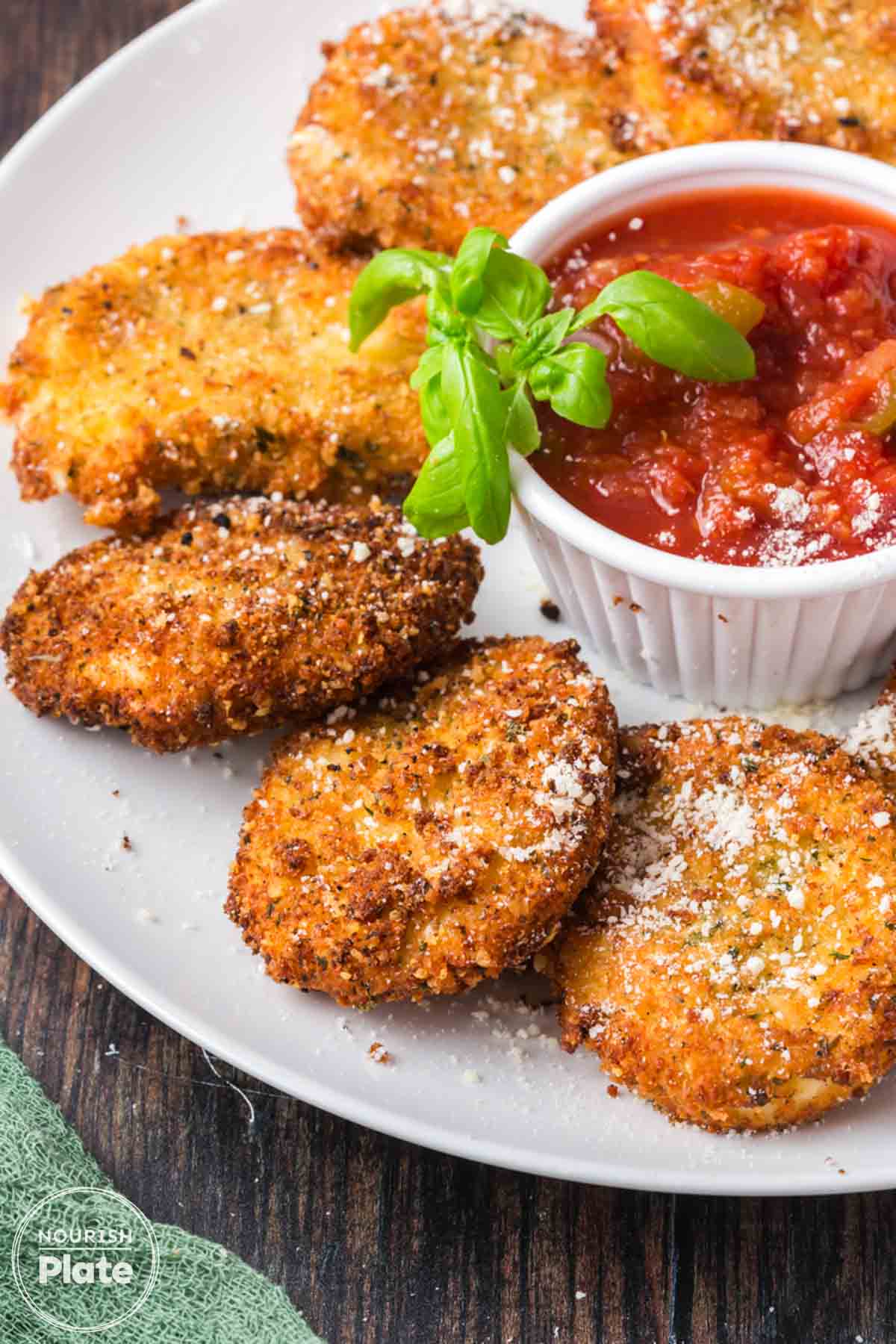 Plate of fried mozzarella cheese slices served with marinara sauce in a small ramekin, topped with basil and finished with a sprinkle of Parmesan cheese.