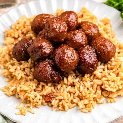 Garlic soy glazed meatballs served over rice on a white plate, with the meatballs coated in a glossy brown sauce.