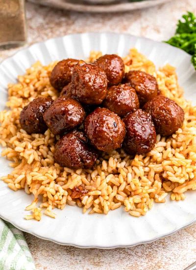 Garlic soy glazed meatballs served over rice on a white plate, with the meatballs coated in a glossy brown sauce.