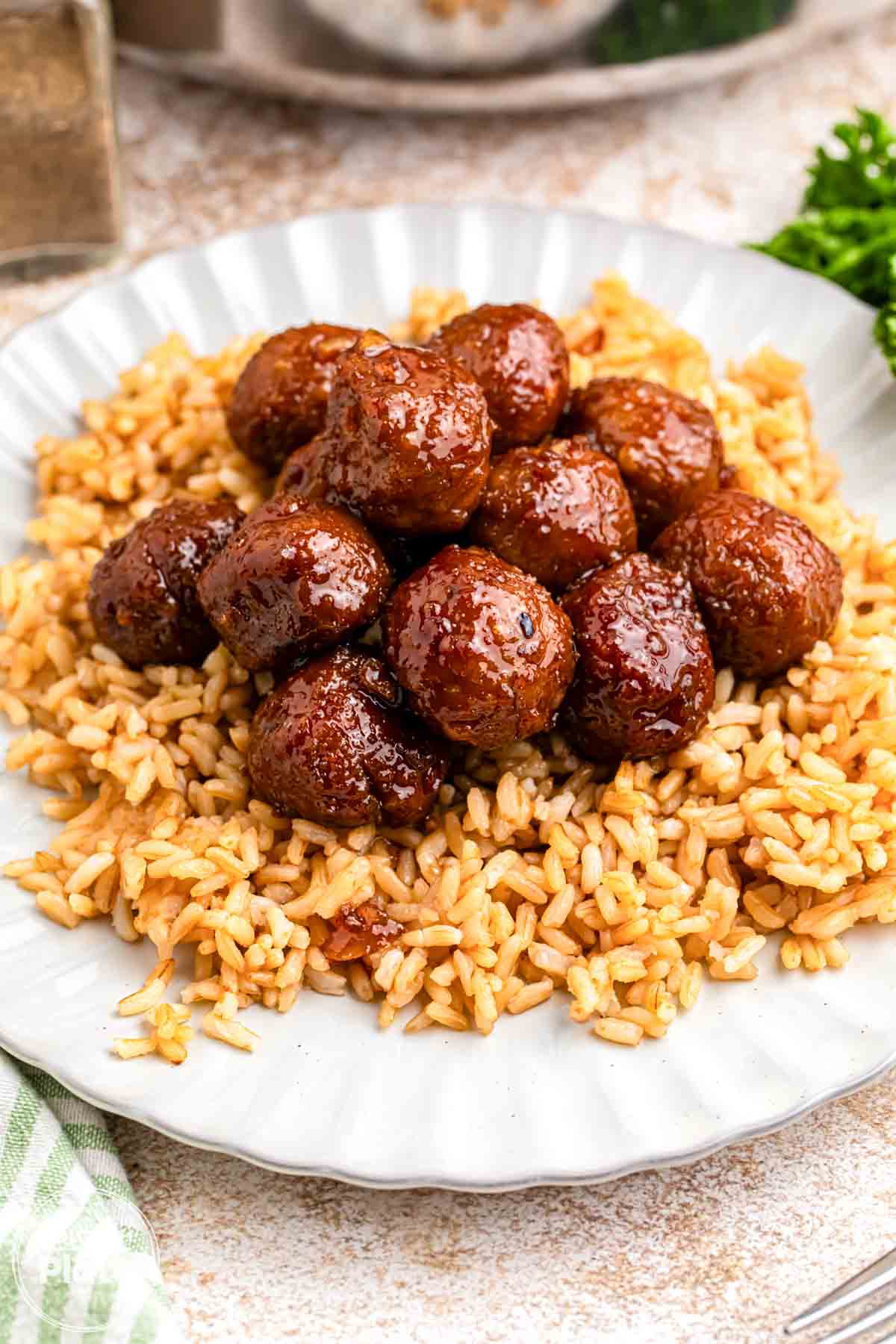 Garlic soy glazed meatballs served over rice on a white plate, with the meatballs coated in a glossy brown sauce.