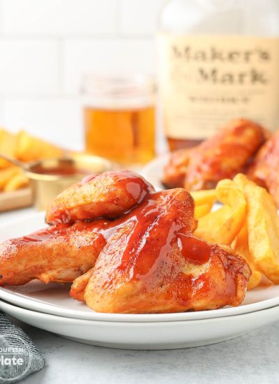 Baked BBQ chicken wings glazed with sauce and served with crinkle-cut fries on a white plate.