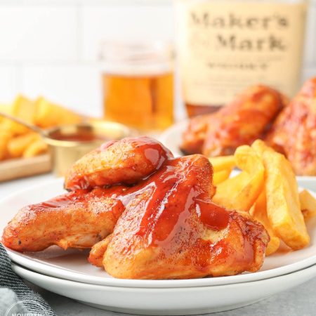 Baked BBQ chicken wings glazed with sauce and served with crinkle-cut fries on a white plate.