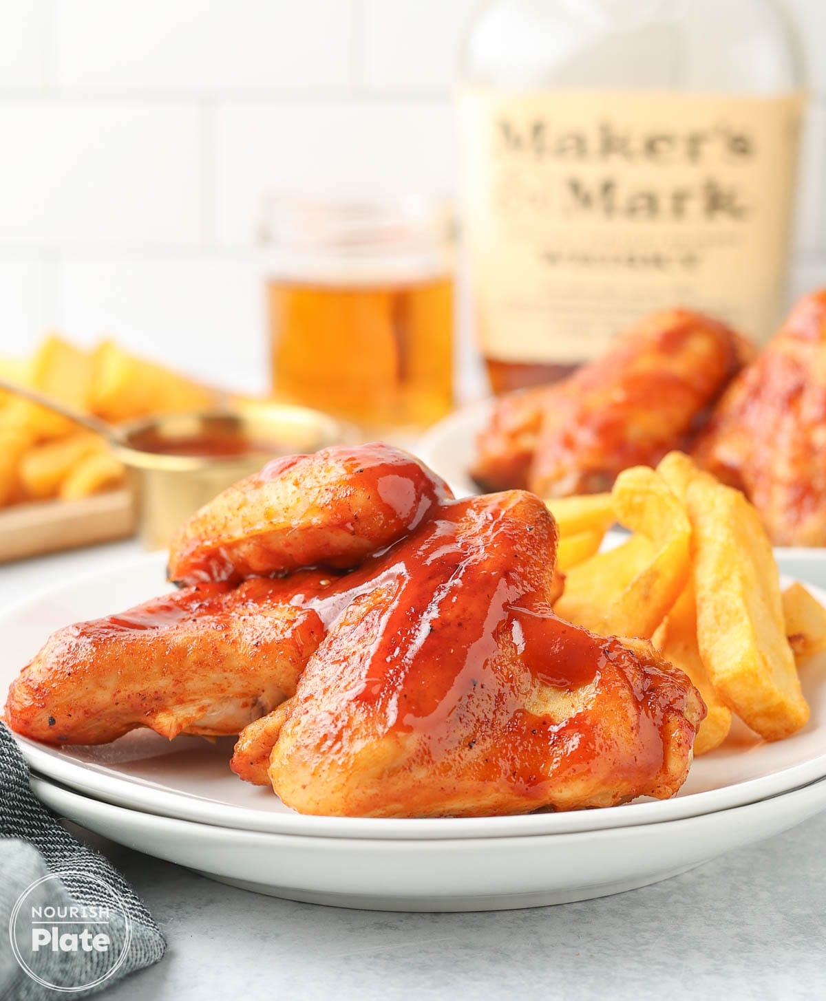 Baked BBQ chicken wings glazed with sauce and served with crinkle-cut fries on a white plate.