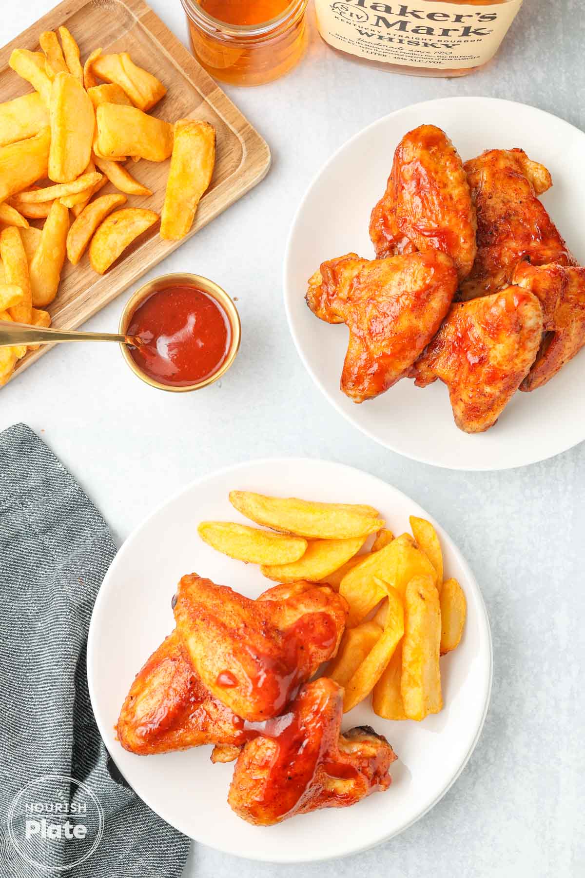 Baked BBQ chicken wings glazed with sauce and served with crinkle-cut fries, with extra BBQ sauce on the side.