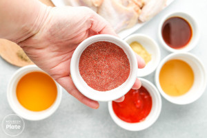Hand holding a bowl of red seasoning mix beside small bowls of barbecue sauce ingredients.