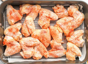 Raw chicken wings sprinkled with red seasoning on a wire rack in a roasting pan.