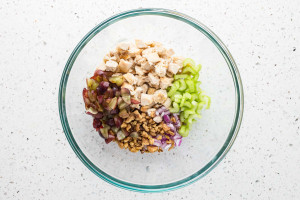 Cooked diced chicken, grapes, celery, walnuts and red onions in a glass bowl.