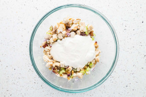 Added white dressing to the chicken salad mixture, in a glass bowl.