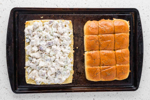 Chicken salad spread over the bottom half of slider rolls, with herb-topped rolls ready to place on top.