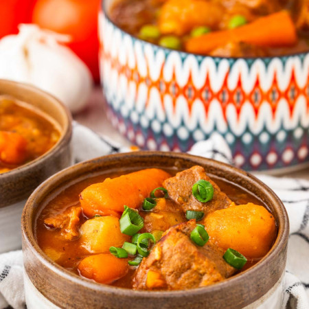 Bowl of Instant Pot beef stew with tender beef, carrots, potatoes, peas, and rich tomato gravy.