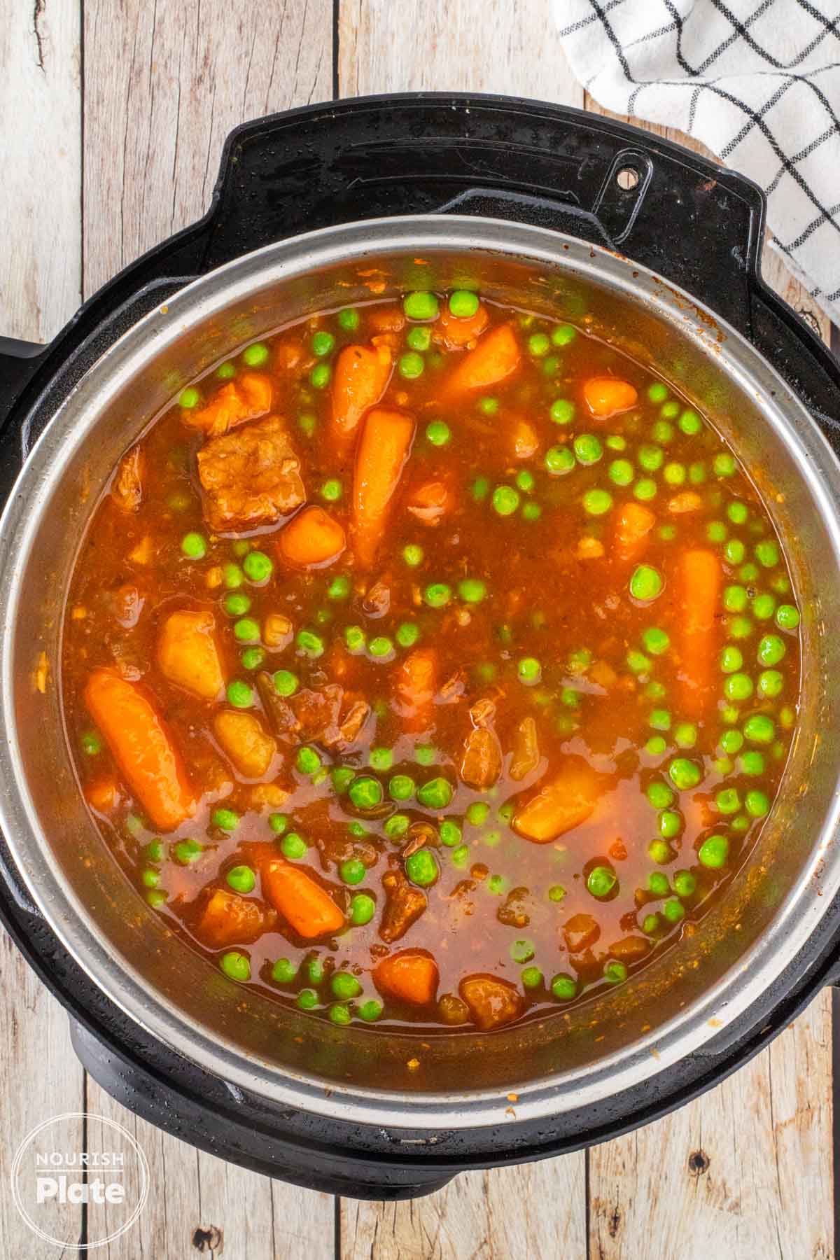 Instant Pot beef stew with tender beef, carrots, potatoes, and peas cooking in a tomato beef gravy.