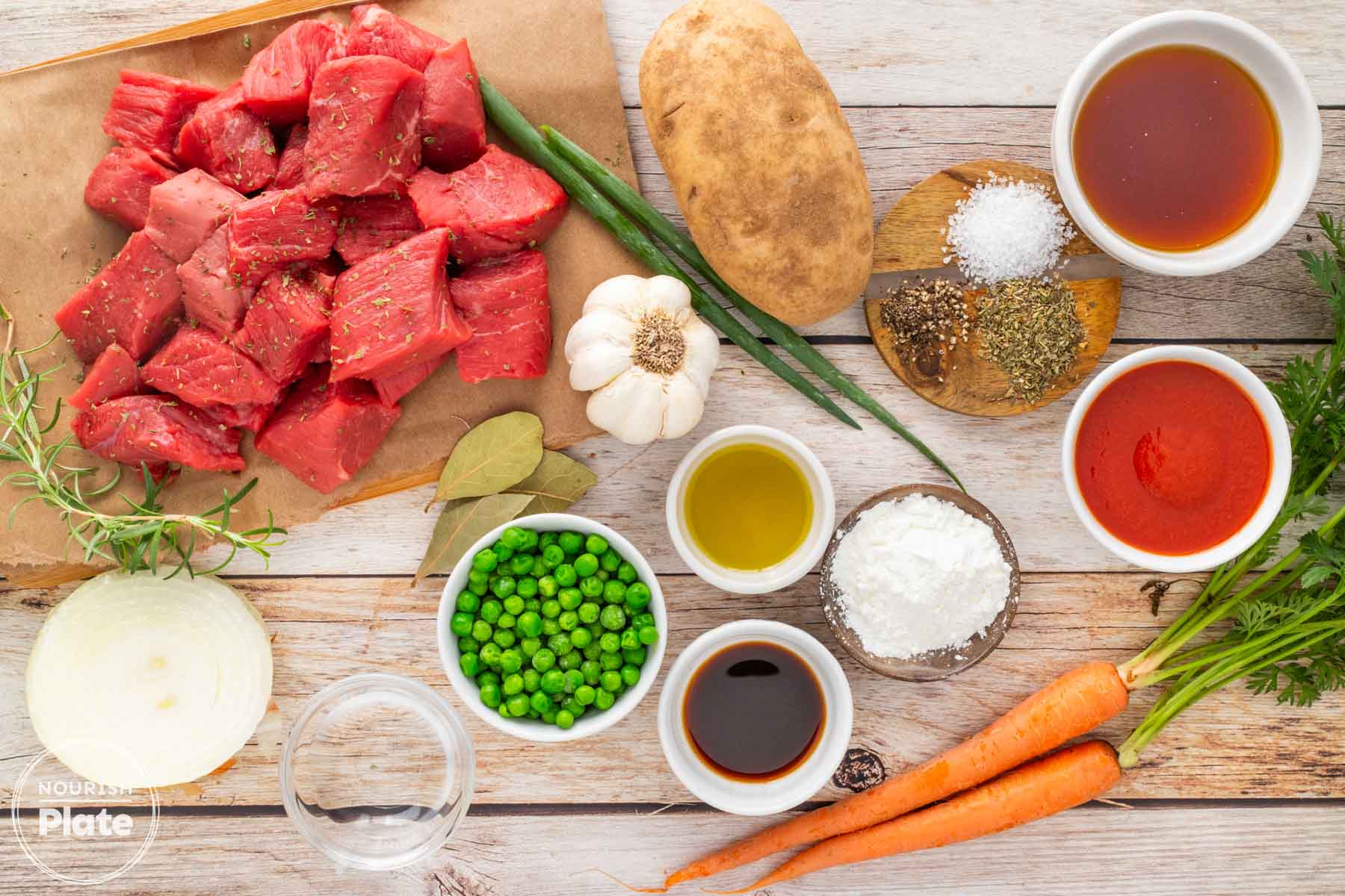 Ingredients for Instant Pot beef stew, including beef cubes, carrots, potatoes, peas, onion, garlic, broth, tomato sauce, and seasonings.