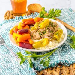 Slow cooker Mississippi pork served over mashed potatoes with baby carrots and pepperoncini