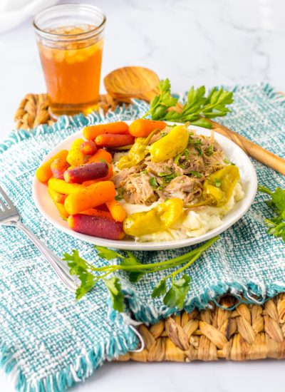 Slow cooker Mississippi pork served over mashed potatoes with baby carrots and pepperoncini