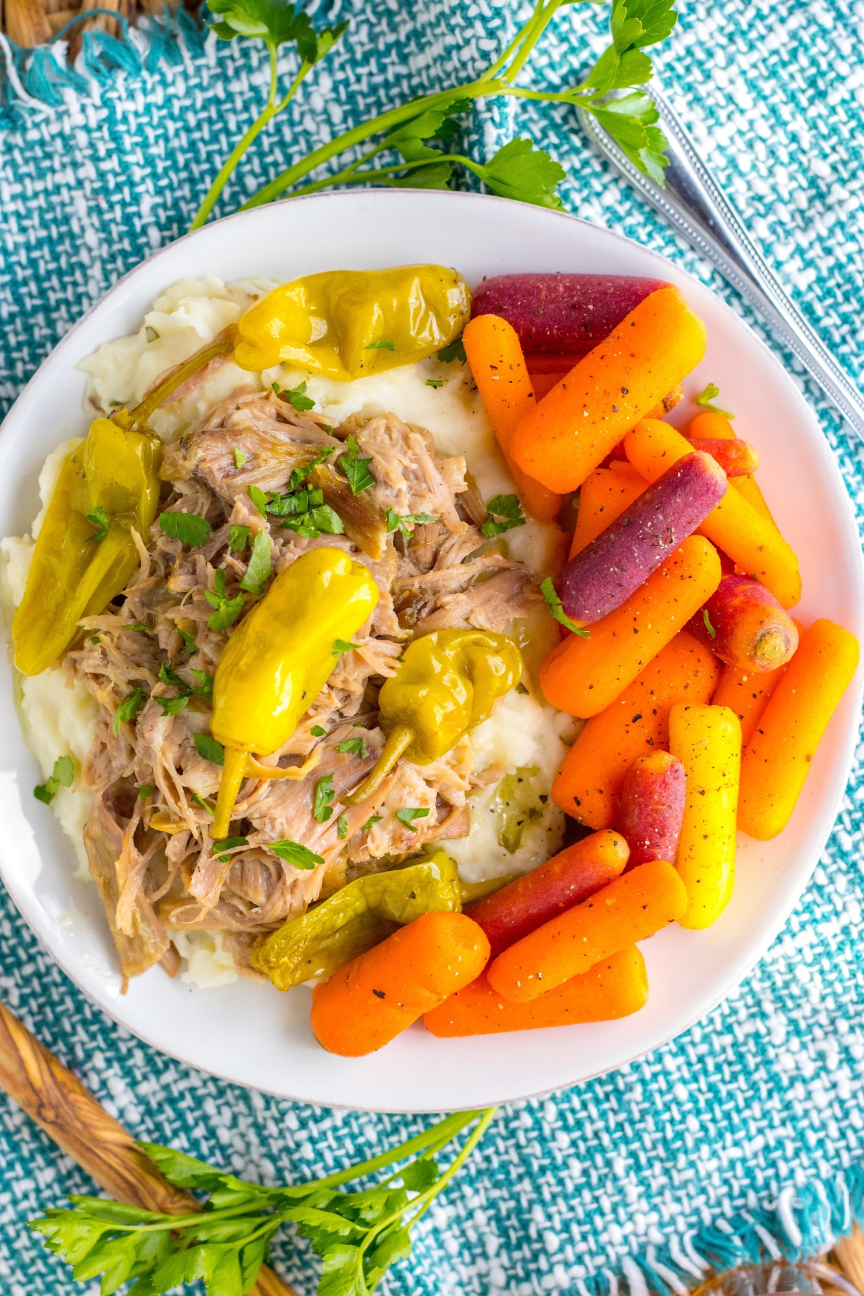 Overhead view of shredded slow cooker Mississippi pork with mashed potatoes and glazed carrots