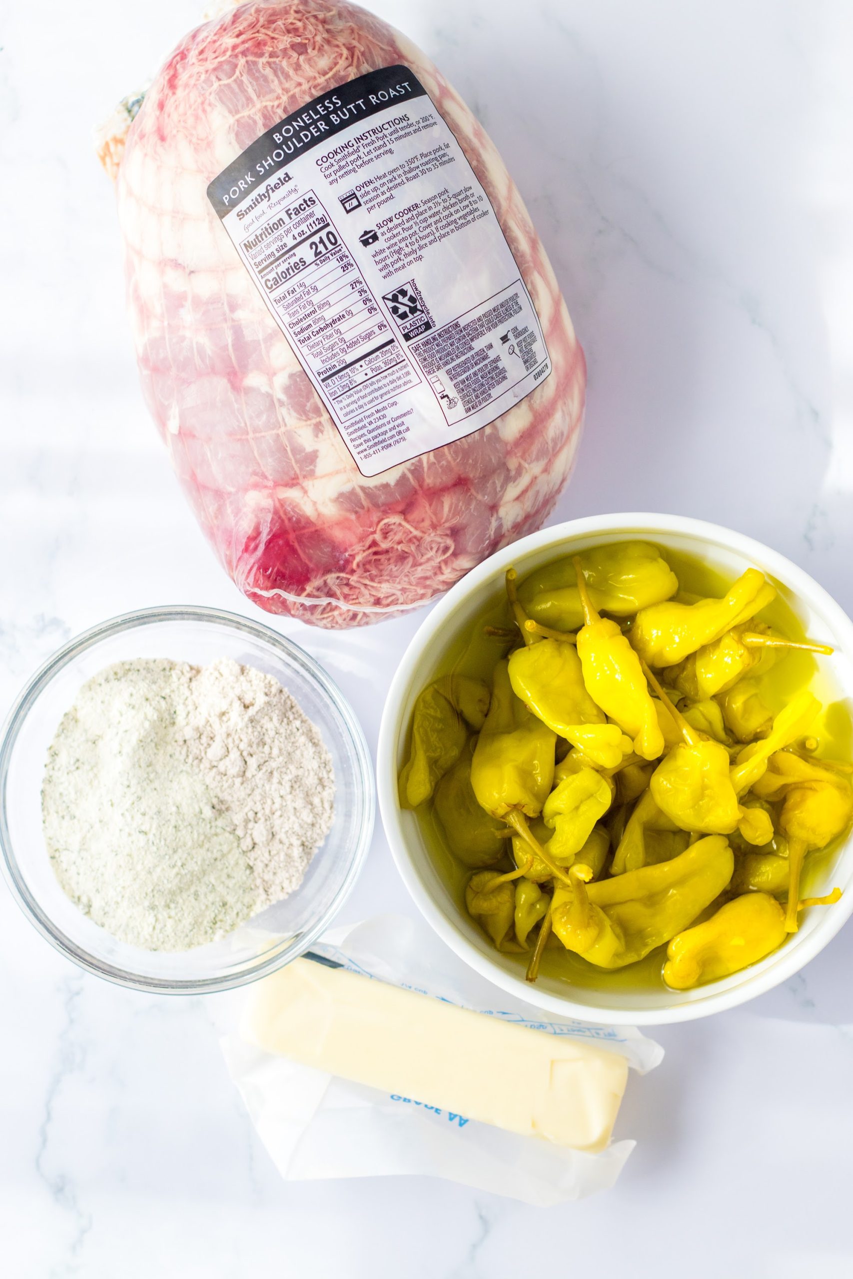 Ingredients for slow cooker Mississippi pork: boneless pork roast, pepperoncini, ranch packet, gravy mix, and a stick of butter