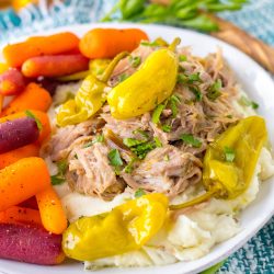Shredded Mississippi pork with pepperoncini over mashed potatoes on a white plate