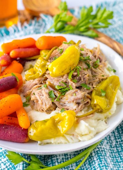 Shredded Mississippi pork with pepperoncini over mashed potatoes on a white plate