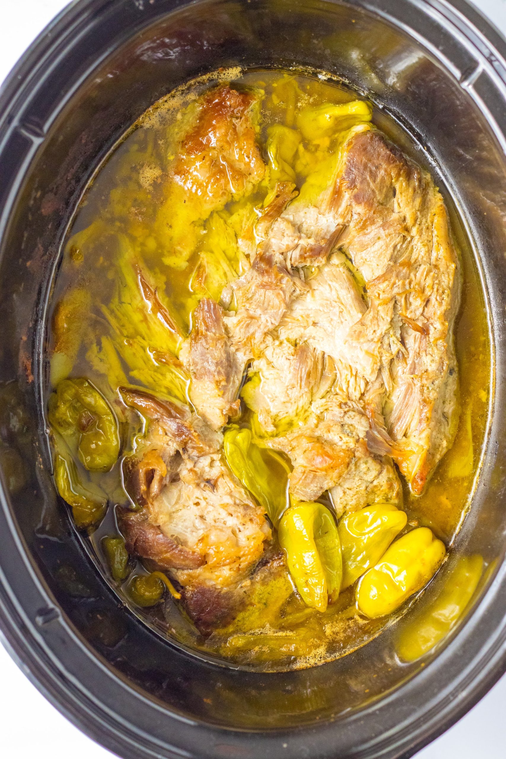 Cooked Mississippi pork roast in the slow cooker surrounded by pepperoncini