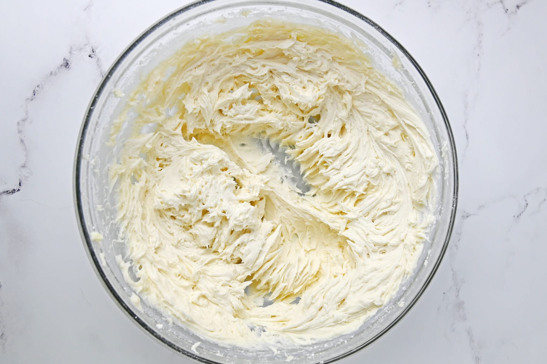 Whipped vanilla buttercream in a glass mixing bowl before coloring
