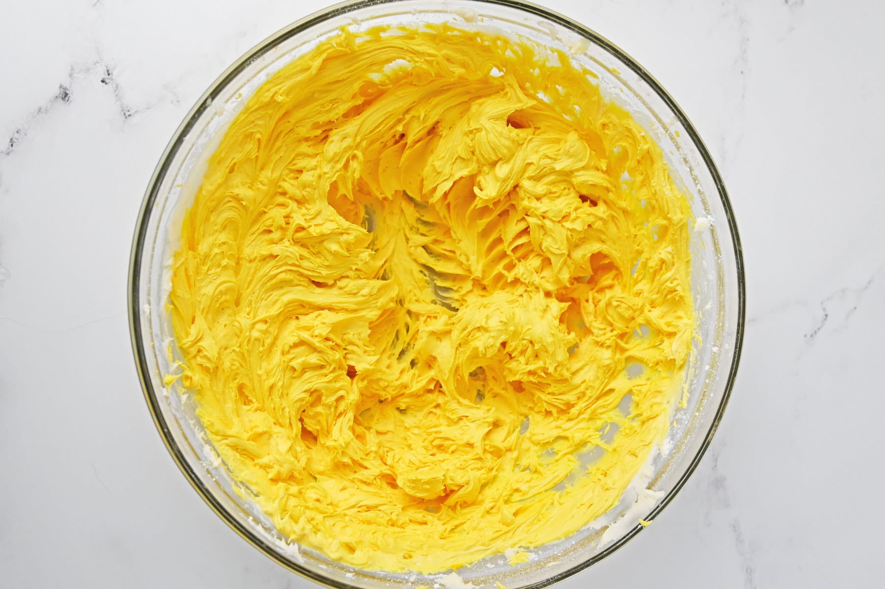 Buttercream frosting colored yellow with gel food coloring in a glass mixing bowl