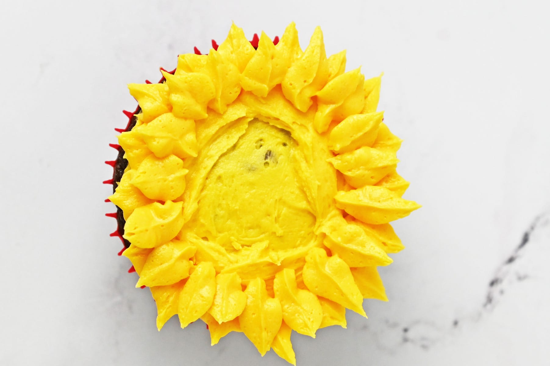 Yellow buttercream petals piped around the edge of a cupcake with the center left open