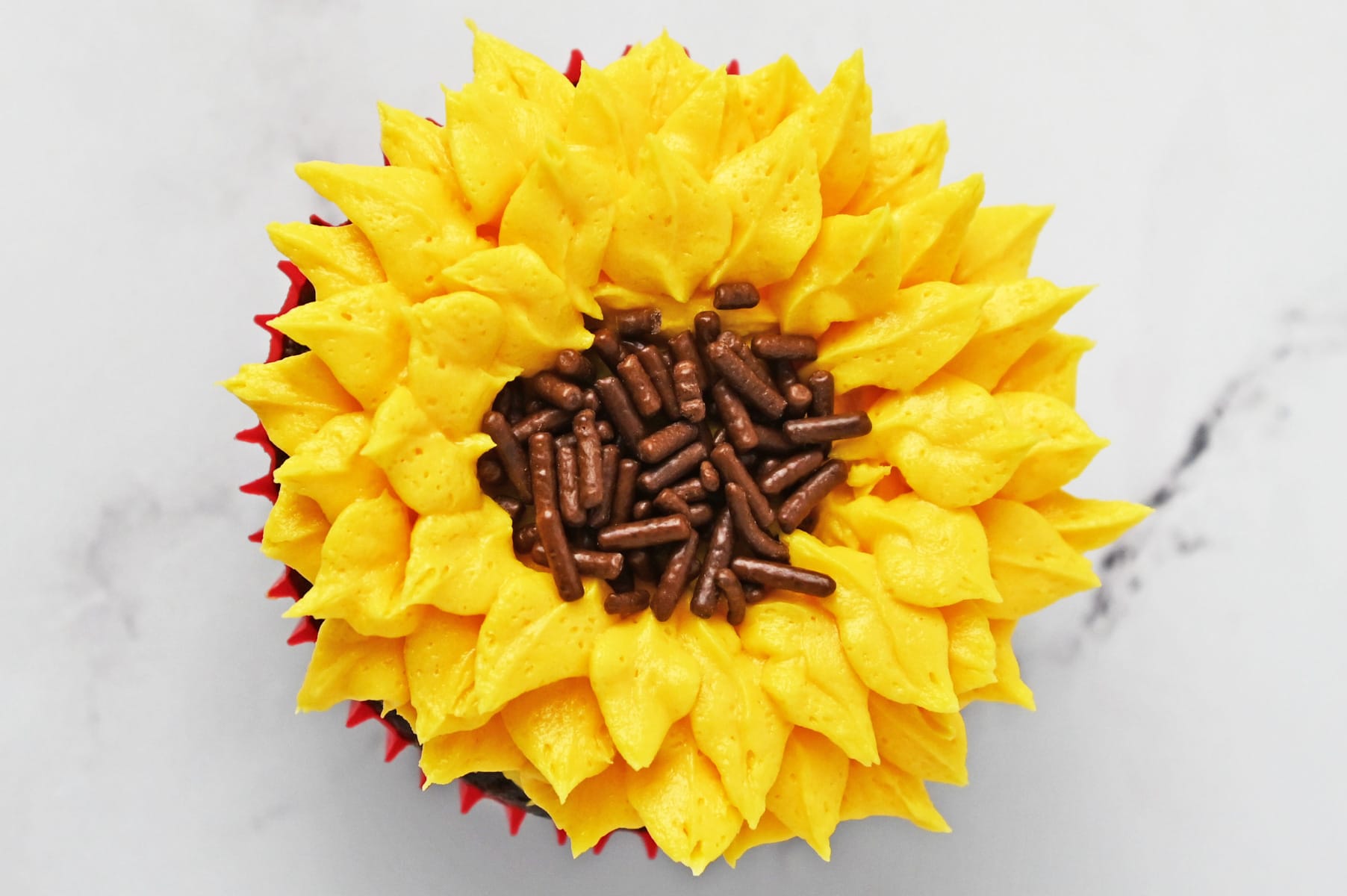 Finished sunflower cupcake with piped yellow buttercream petals and a chocolate sprinkle center
